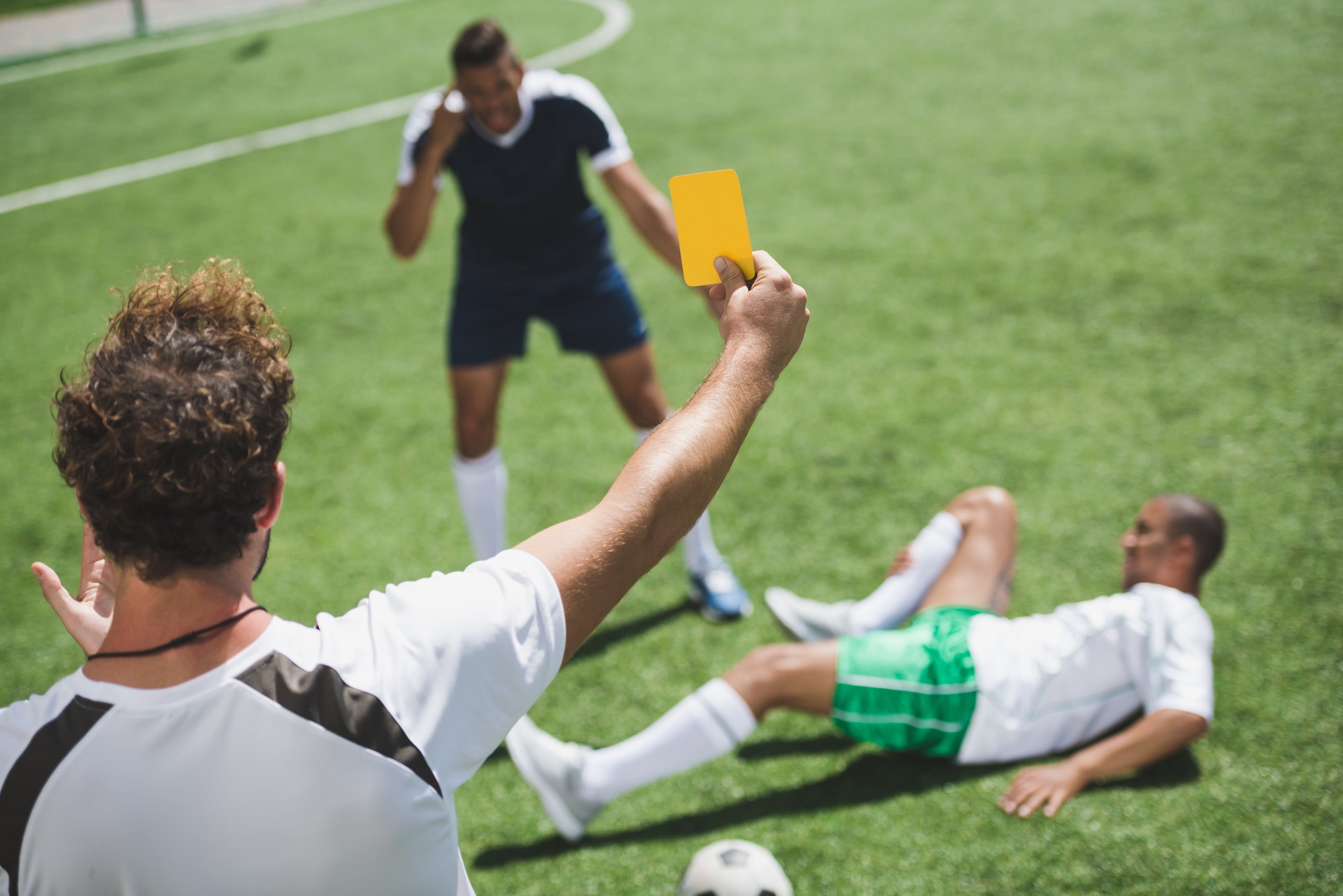back view of soccer referee showing yellow card to players during game